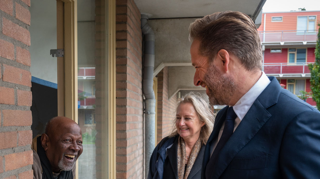 Minister Hugo de Jonge en een vrouw lachen naar een man die uit het raam hangt